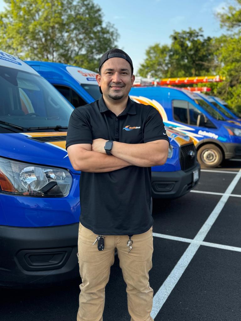 A SwiftPro technician standing arms crossed in front of a row of wrapped SwiftPro vans in Northern Virginia