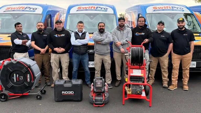 Nine SwiftPro plumbers in front of three wrapped SwiftPro vans in Northern Virginia, with a RIDGID drain cleaning machine, sewer camera and water jetter