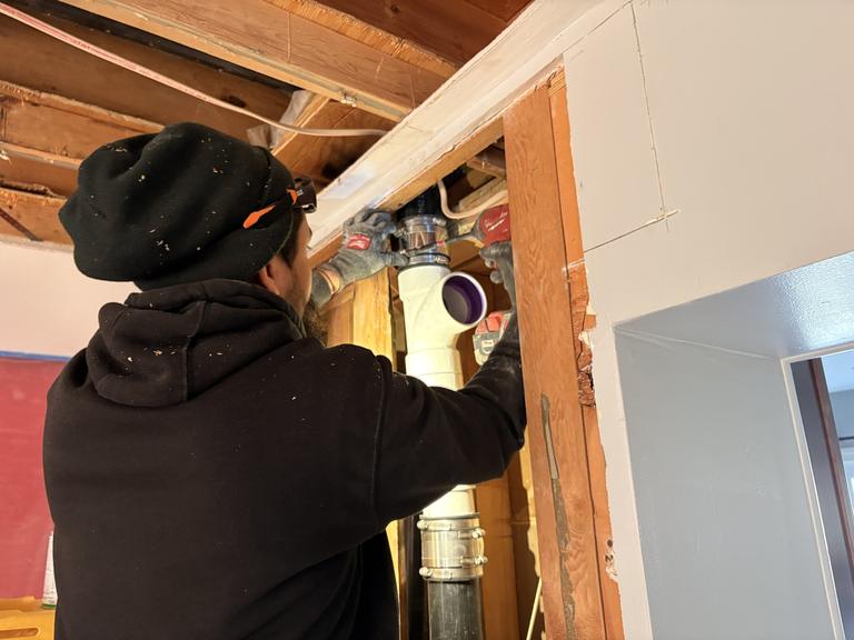 A SwiftPro plumber fitting a new PVC drain stack inside an opened wall in a Northern Virginia home