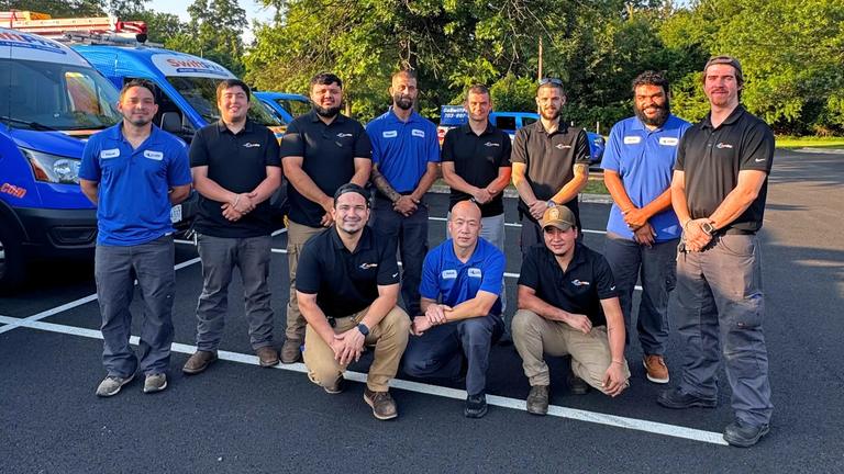 Eleven SwiftPro HVAC and plumbing technicians in company polos standing and kneeling beside wrapped SwiftPro vans in Northern Virginia