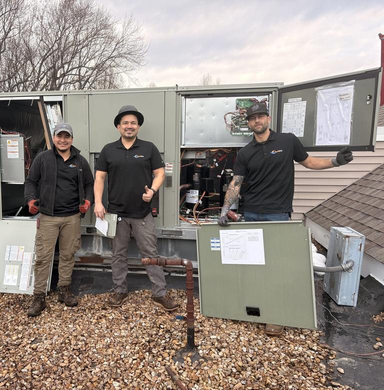 Three SwiftPro HVAC technicians smiling on a flat roof in Northern Virginia beside a rooftop unit with its service panels open