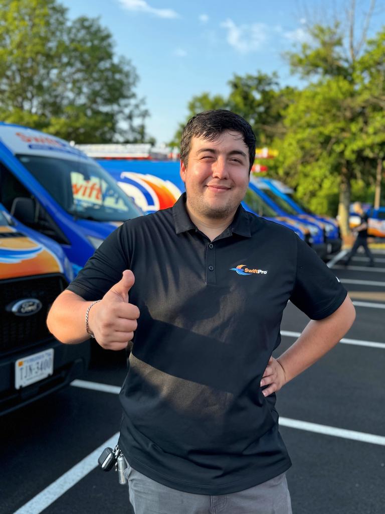 A SwiftPro technician in a company polo giving a thumbs up beside the wrapped SwiftPro vans in Northern Virginia